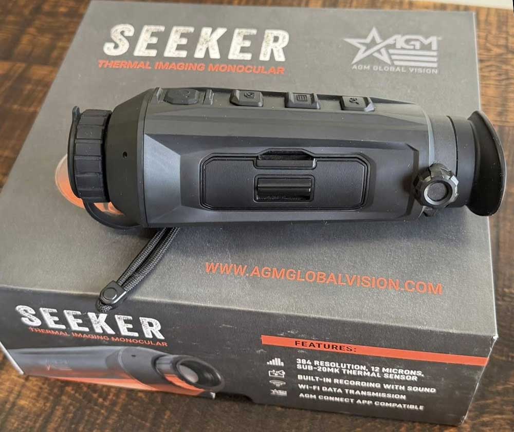 Фото тепловізора AGM Seeker 15-384 на фоні тактичного спорядження для демонстрації компактності та ергономіки